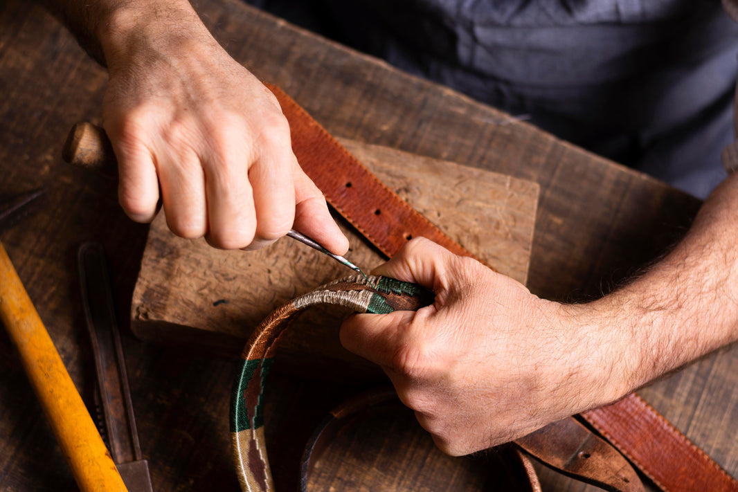 Person working on a leather belt with tools on a wooden surface