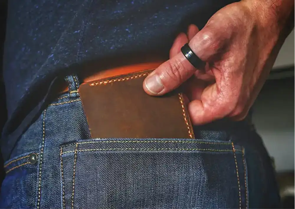 Hand pulling a brown leather wallet out of a blue jeans pocket.